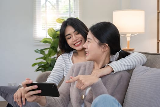 Asian lesbian couple enjoying time together at home on the sofa. Concept of love, togetherness, and intimate moments in a cozy indoor setting.