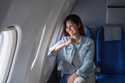 Asian woman smiling while sitting by airplane window. Concept of air travel, relaxation, and leisure.