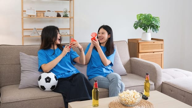 A lesbian couple cheers football and celebrate together for their favorite Euro football team. A young female couple cheers football on TV together in the living room on match day..