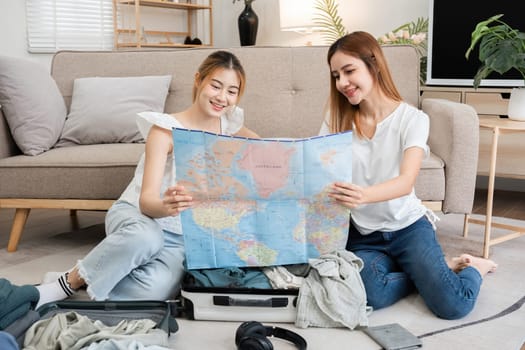 Asian women planning trip with map and suitcase in living room. Concept of travel preparation and adventure..