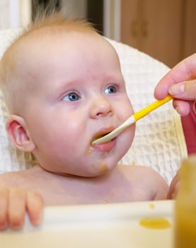 Mom feeding little boy with broccoli puree. Child at the age of six months eats broccoli while sitting on a baby chair.