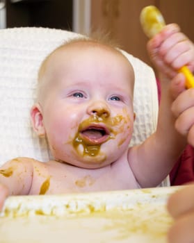 Mom feeding little boy with broccoli puree. Child at the age of six months eats broccoli while sitting on a baby chair.