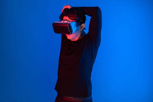 Smart sportman player wearing VR stretching whole body posing on blue neon light background connecting digital futuristic technology virtual reality metaverse world in exercise concept. Contrivance.