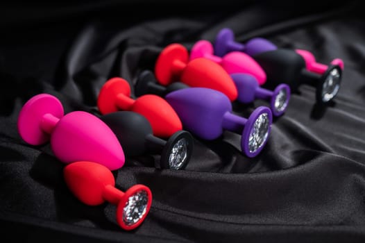 A set of silicone anal plugs in different colors and sizes on a black silk sheet