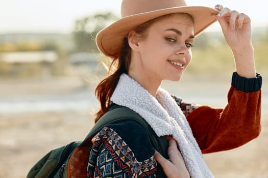 Stylish woman in hat and sweater posing with backpack on shoulder in outdoor setting