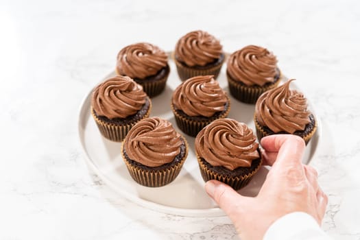 Freshly baked cupcakes have been masterfully infused with rich caramel and adorned with velvety chocolate frosting, all elegantly presented on a pristine white serving plate.