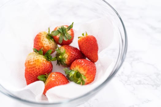 Freshly washed and dried strawberries are carefully arranged in a glass bowl lined with paper towel, ready for snacking or further use.