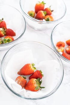 Bright red strawberries, interspersed with signs of mold, rest in a glass bowl lined with a paper towel on a white napkin, indicating improper storage techniques.