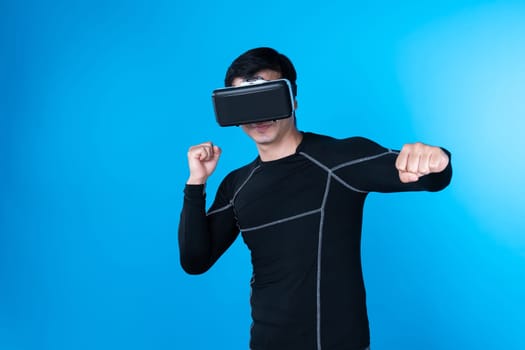 Smiling smart boxing gamer wearing VR playing boxer game to punch camera posing isolated blue background connecting futuristic technology virtual reality in meta fighting box stadium. Contrivance.