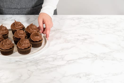 Freshly baked cupcakes have been masterfully infused with rich caramel and adorned with velvety chocolate frosting, all elegantly presented on a pristine white serving plate.