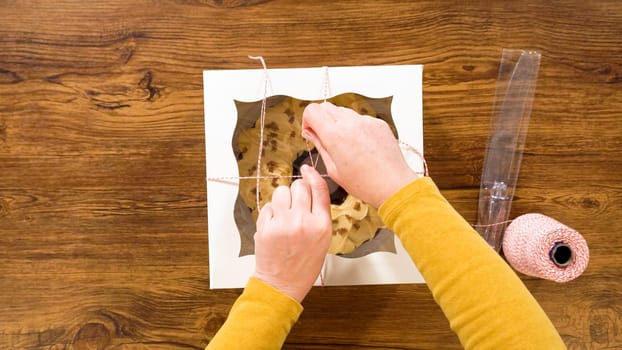 Flat lay. Carefully placing the gingerbread bundt cake, adorned with salted caramel frosting and gingerbread sprinkles, into a white paper bundt cake box with a clear window for gifting.