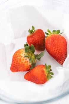 Freshly washed and dried strawberries are carefully arranged in a glass bowl lined with paper towel, ready for snacking or further use.