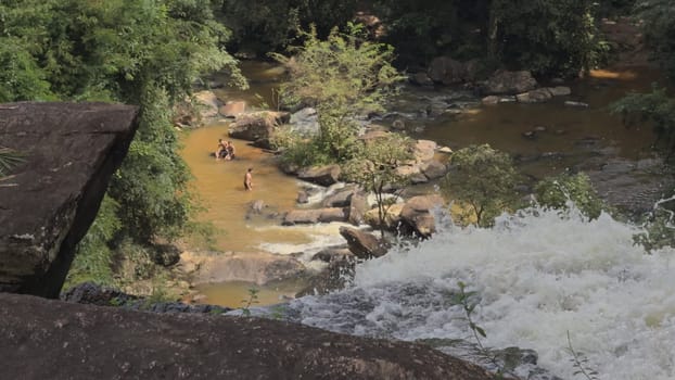 A waterfall in a jungle with people swimming in brown waters below.