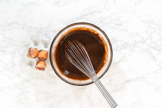 Flat lay. In the process of creating mouthwatering chocolate cupcakes, the first step involves meticulously mixing the ingredients in a glass mixing bowl to make the perfect batter.