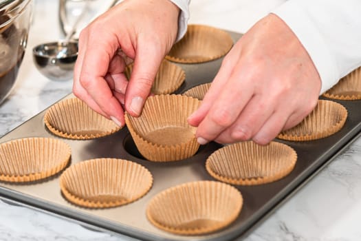 Getting ready to bake delicious chocolate cupcakes, we carefully line the cupcake pan with paper liners, ensuring a delightful treat awaits.