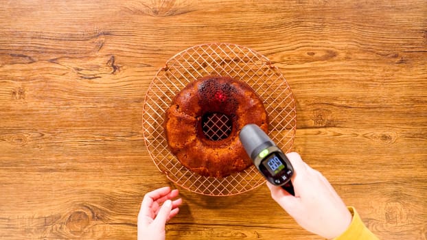 Flat lay. A baker meticulously checks the temperature of a freshly baked Gingerbread Bundt Cake, which will soon be adorned with smooth, rich caramel frosting. The cake's dark, molasses-infused crumb contrasts with the rustic wood surface, hinting at the spicy, warm flavors that pair perfectly with the sweet frosting.