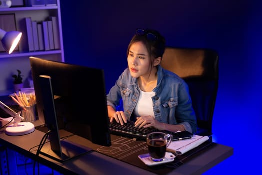 Stressful young beautiful asian creative looking on pc to search project creator social media online with planning channel strategy reach of more viewer home at neon modern office at night. Stratagem.