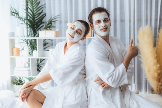 Blissful couple in bathrobe with facial cream mask enjoying serene ambiance of spa salon resort or hotel during holiday. Pampering face spa and skincare treatment with essence relaxation. Quiescent