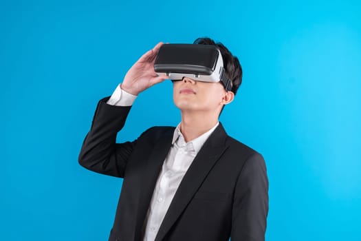 Smiling Asian businessman looking thorough VR connecting to business world report in futuristic metaverse, analyzing innovation technology ads in virtual reality isolated blue copyspace. Contrivance.