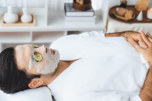 Serene daylight ambiance of spa salon, man customer indulges in rejuvenating with luxurious cucumber facial mask. Facial skincare treatment and beauty care concept. Quiescent