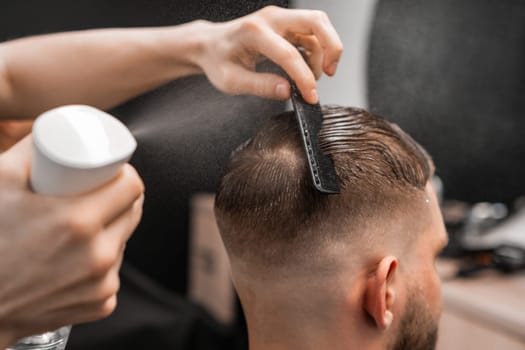 Barber spritzes and combs a ma's hair, adding finesse to the style at the barbershop.