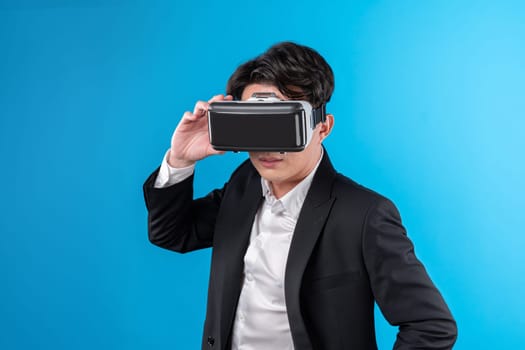 Smiling Asian businessman looking thorough VR connecting to business world report in futuristic metaverse, analyzing innovation technology ads in virtual reality isolated blue copyspace. Contrivance.