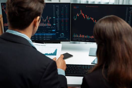 Two business traders discussing on dynamic stock market in currency rate investment trading on two pc screens with compare real time graph on risk or profit point of data at modern office. Postulate.