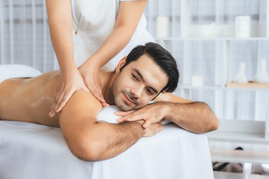 Caucasian man customer enjoying relaxing anti-stress spa massage and pampering with beauty skin recreation leisure in day light ambient salon spa at luxury resort or hotel. Quiescent