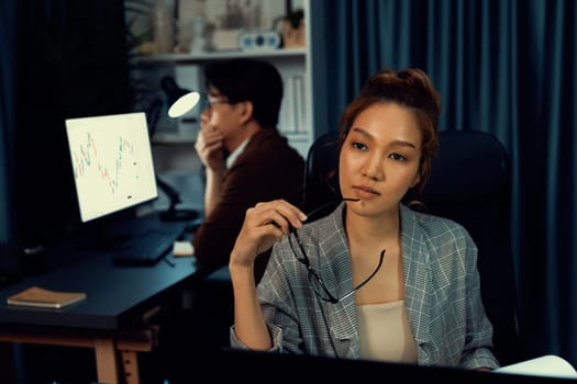 Stressful businesswoman looking at computer stock exchange via email with coworker working at back position talking to ask problem with loss profit on time at modern home office at night. Infobahn.