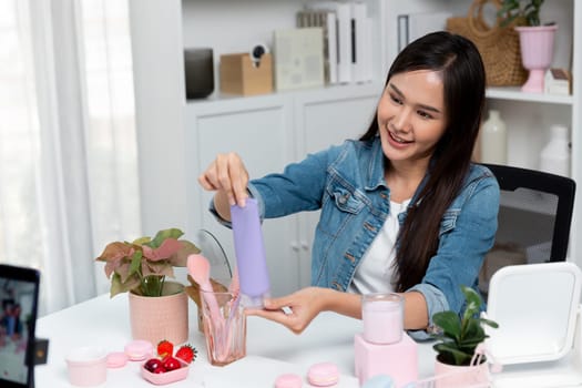 Young beautiful Asian girl reviewing moisturizing body lotion cream product to make glow skin testing on arm on social media online live recording smartphone with bestseller at modern room. Stratagem.