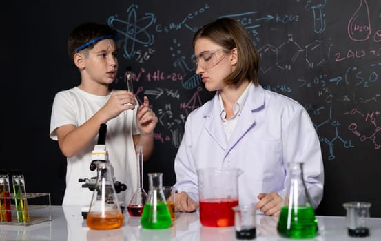 Teacher support schoolboy in laboratory. Schoolboy and teacher stand and experiment about science of chemistry in STEM class using liquid in glass container. Instructor mixing solution. Erudition.