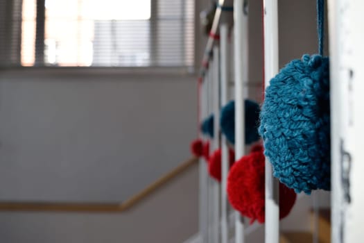 Close-up of colorful yarn pom-poms hanging on a staircase railing with a blurred background.