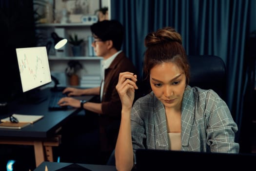 Serious face of thinking businesswoman focusing computer to report data analysis social media online project job with coworker working at back side at over late night time at modern office. Infobahn.