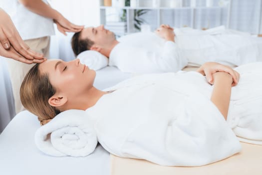 Caucasian couple enjoying relaxing anti-stress head massage and pampering facial beauty skin recreation leisure in dayspa modern light ambient at luxury resort or hotel spa salon. Quiescent