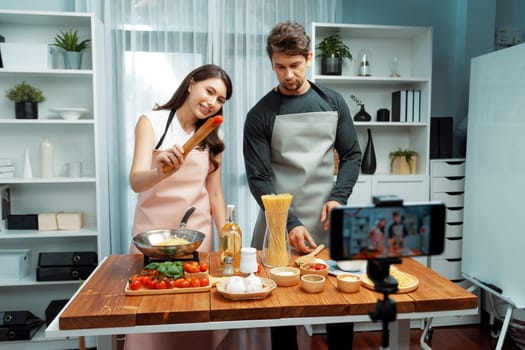 Couple chef influencers cooking special homemade of spaghetti mix ingredient taking to frying pan, putting seasoning and tasty sauce to make good flavor, recording on smartphone on chanel. Postulate.