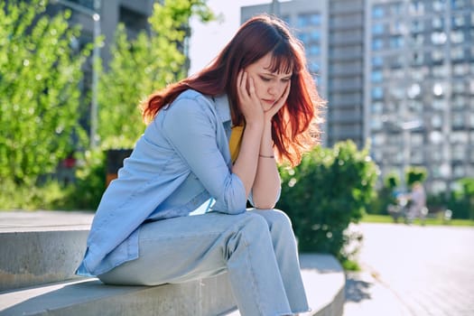 Upset sad unhappy young female sitting outdoor on steps. Girl university college student sitting, holding head with hands. Problems, difficulties, depression, mental health of young people