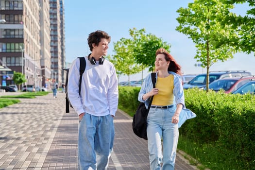 Talking walking friends, guy and girl, university college students walking together along street of modern city. Youth 19-20 years old, friendship, communication, urban lifestyle concept