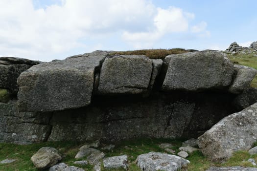 Large granite boulders stacked together in a natural formation on a grassy hillside under a partly cloudy sky.