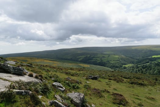 A scenic view of a hilly landscape with green fields, rocky outcrops, and a cloudy sky.