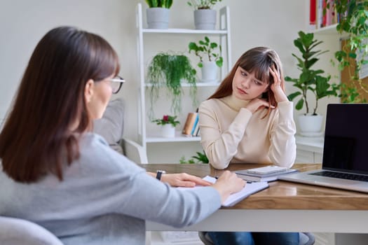 Sad upset teenage girl talking to psychotherapist psychologist counselor at therapy session in specialist office. Mental health of youth, social services for mental support, psychological counseling