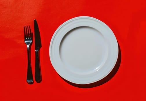 Top view of empty plate with fork and knife on red background, copy space for travel food blog