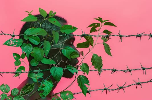Man standing behind barbed wire fence with green plants in front of him, representing freedom and nature in confinement