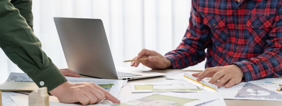 Professional architect design a blueprint by using laptop during project manager shows mistake point on table with architectural document and wooden block scatter around.. Closeup. Delineation.