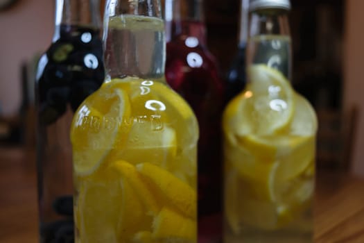 Four glass bottles filled with different types of infused gin, including lemon and berry flavors, placed on a wooden table.