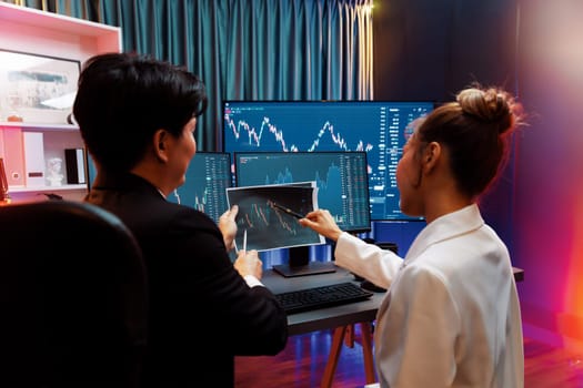 Asian businessman showing dynamic stock exchange graph paper with partner to discuss profit value online investment on website program application, analyzing report at neon light at night. Infobahn.