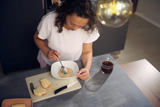 Healthy eating, slimming and diet concept. Curly haired brunette, multi ethnic woman eating healthy muesli for breakfast in the morning. Nearby a cup of freshly brewed coffee on the kitchen counter