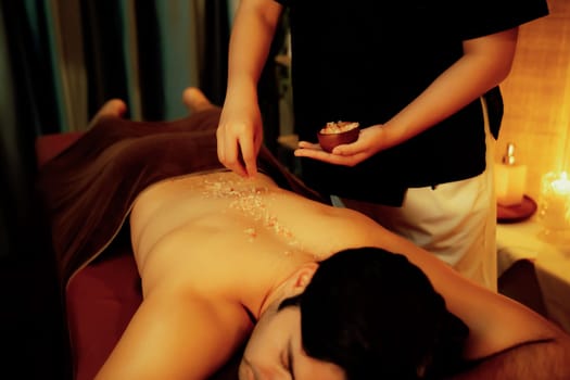 Man customer having exfoliation treatment in luxury spa salon with warmth candle light ambient. Salt scrub beauty treatment in Health spa body scrub. Quiescent