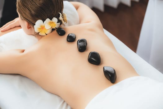 Hot stone massage at spa salon in luxury resort with day light serenity ambient, blissful woman customer enjoying spa basalt stone massage glide over body with soothing warmth. Quiescent