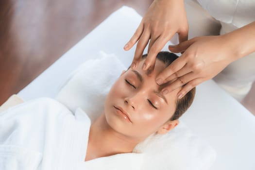 Caucasian woman enjoying relaxing anti-stress head massage and pampering facial beauty skin recreation leisure in dayspa modern light ambient at luxury resort or hotel spa salon. Quiescent