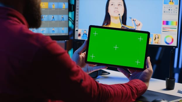 Photo editor uses green screen tablet to watch online podcast while looking at pictures taken with professional camera. Freelancer in home studio browsing images and looking at videos on mockup device
